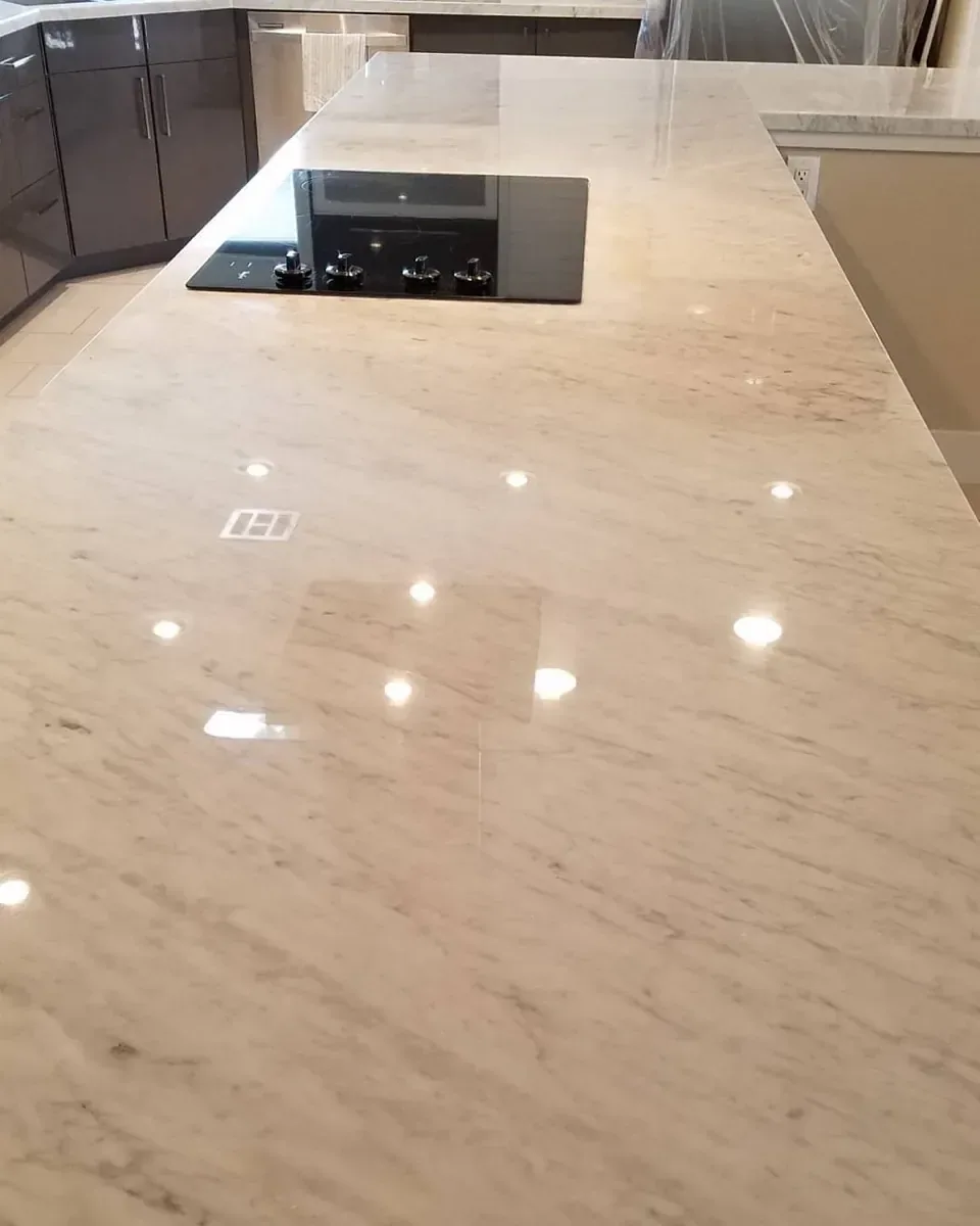 White Carrara marble kitchen island with an even polished finish reflecting the ceiling lights