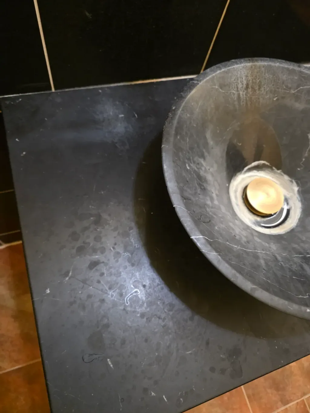 Dull, cloudy etch marks scattered across a dark marble vanity top beside a stone vessel sink