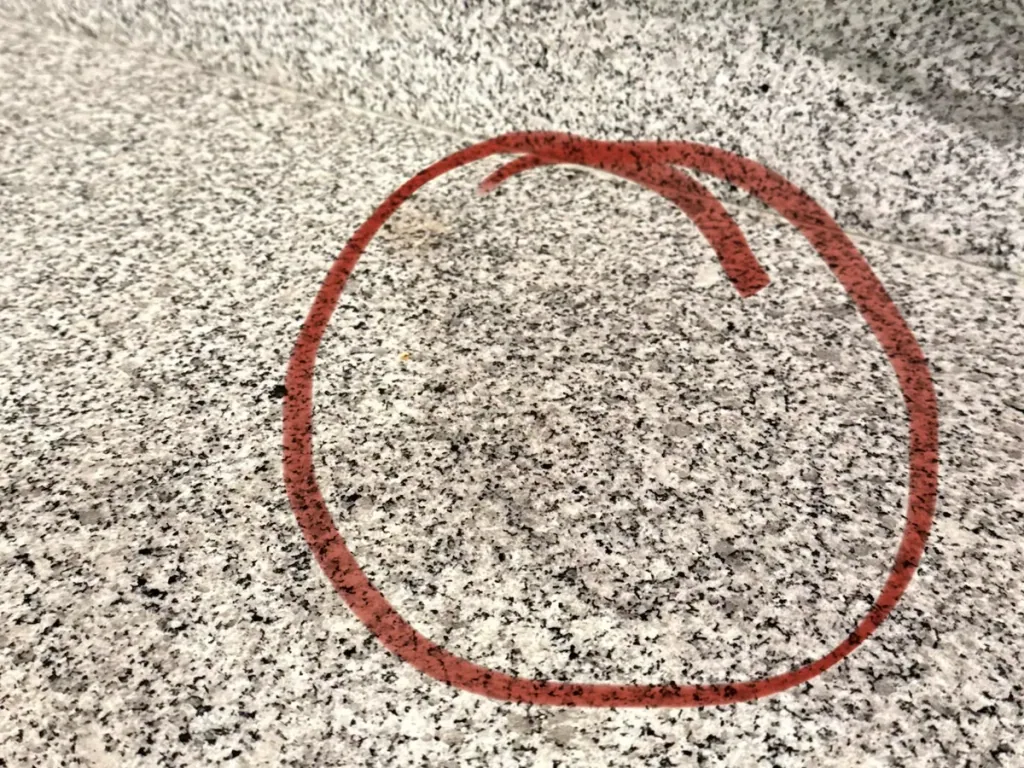 Darker patch on a light gray speckled granite countertop where an appliance sat, circled in red