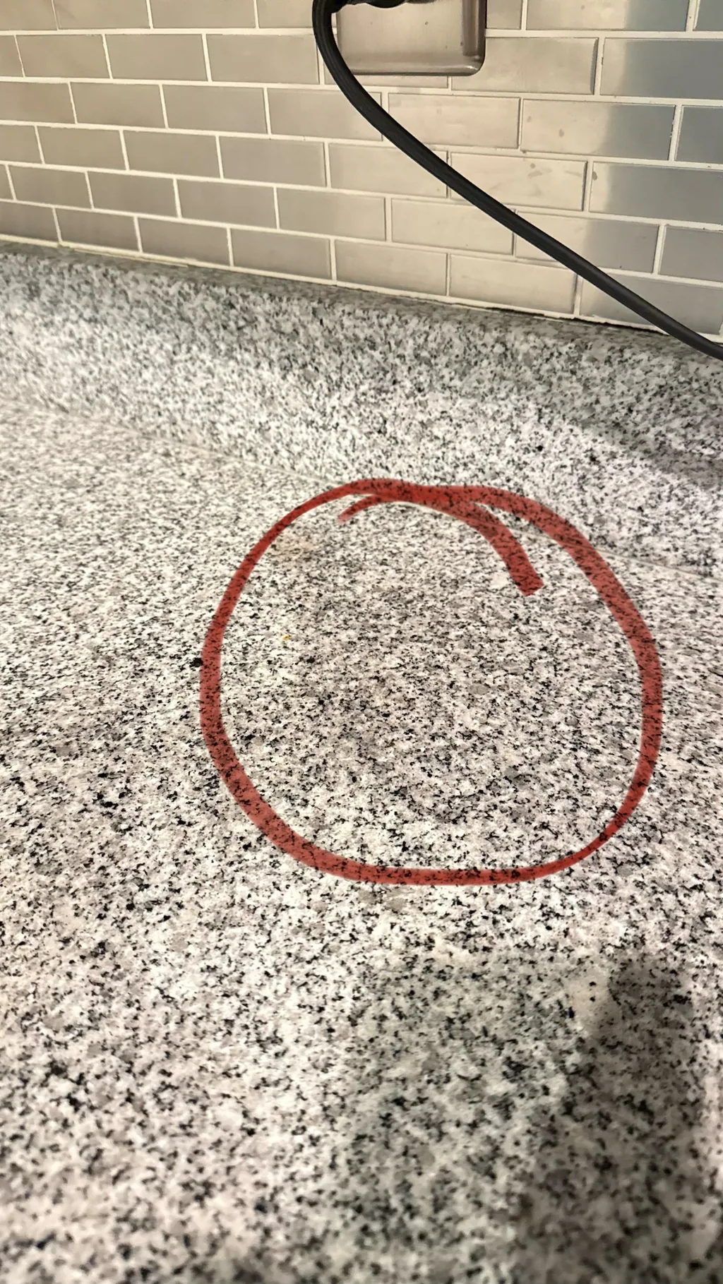Dark area on a speckled granite countertop where an espresso machine sat, marked with a red circle