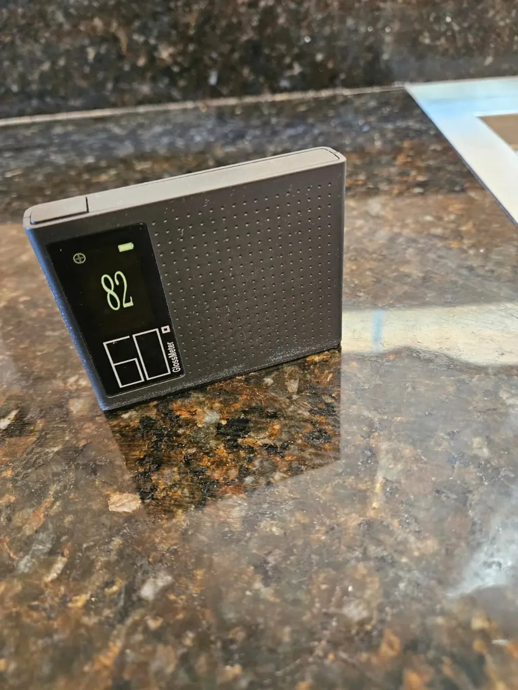 Gloss meter reading 82 on a dark brown granite countertop before polishing