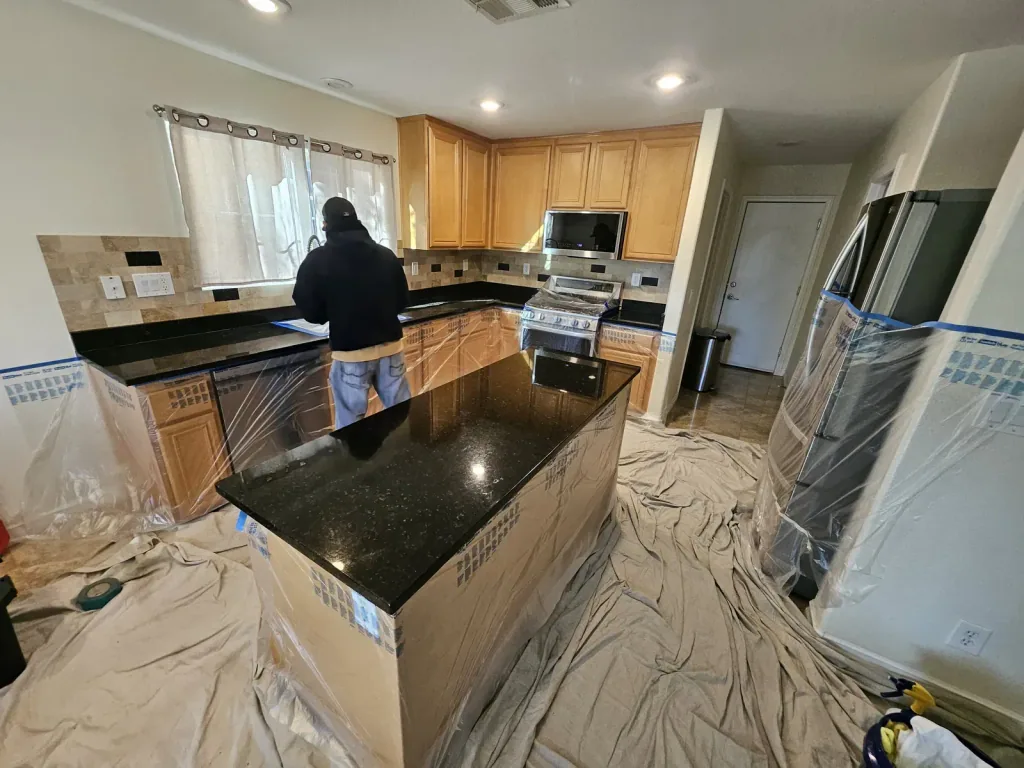 Dark granite kitchen island being polished with the cabinets and floor covered in protective sheeting