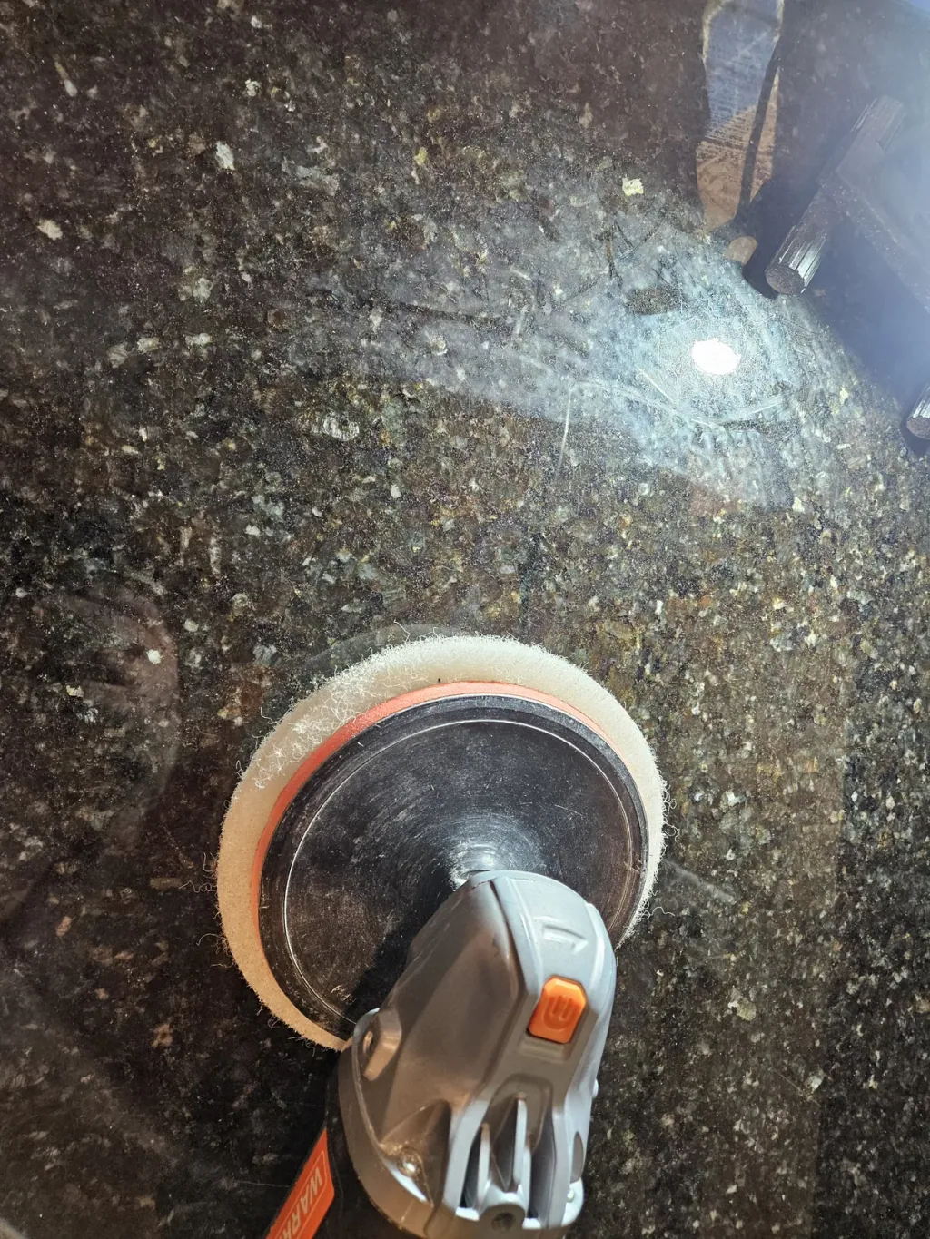 Polishing pad on a hand polisher working the surface of a dark speckled granite countertop