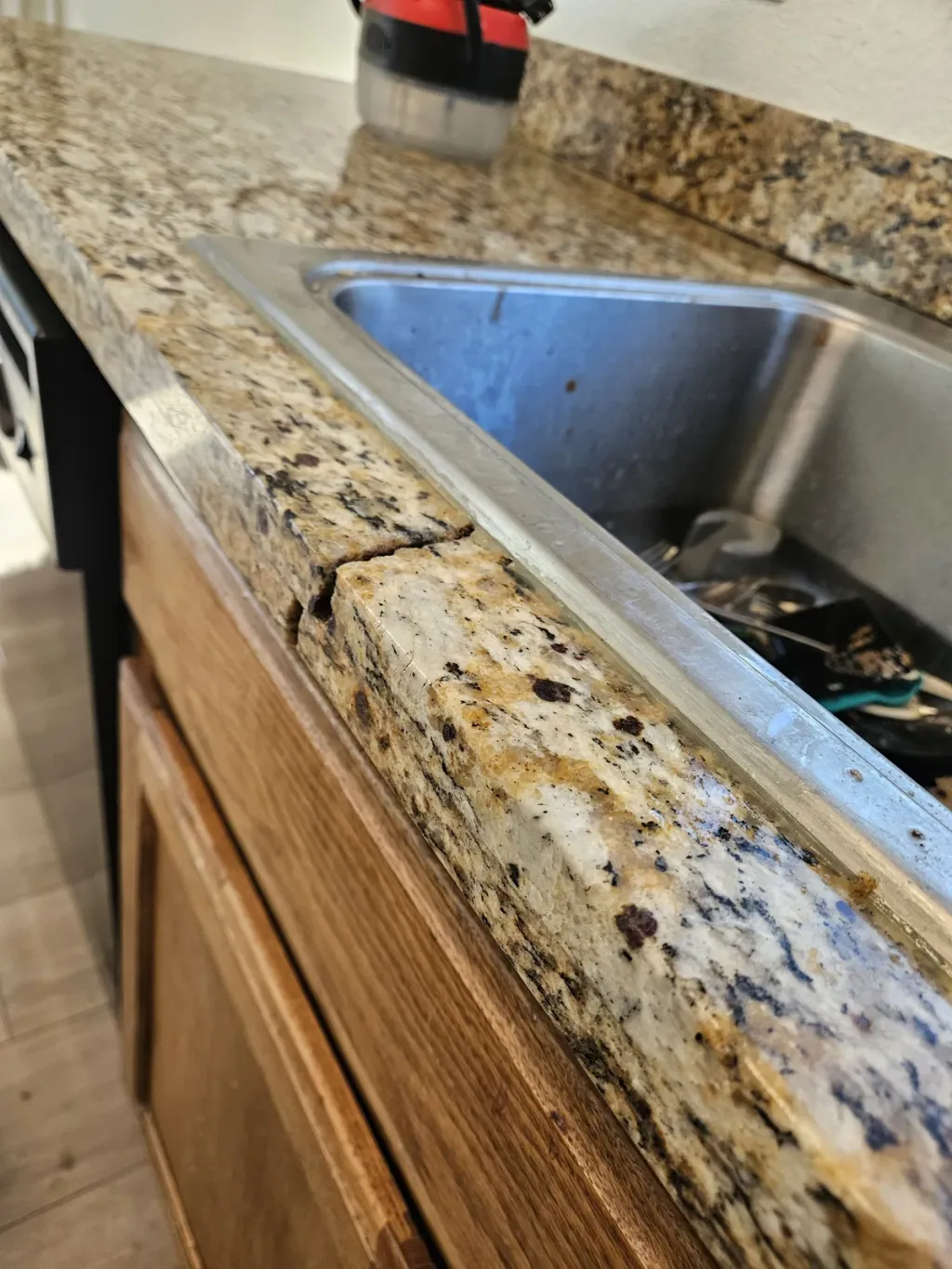 Crack running across the front edge of a speckled granite countertop beside an undermount sink