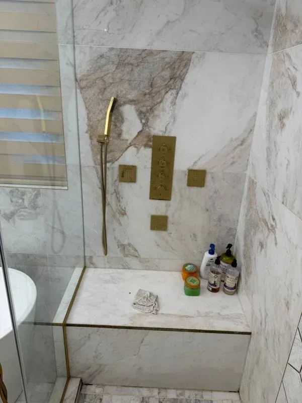 Marble shower wall with a large veined slab, brass shower controls, and a marble bench