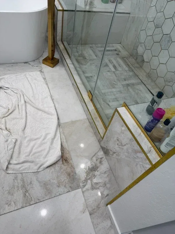 Polished marble bathroom floor and shower curb with brass trim beside a freestanding tub