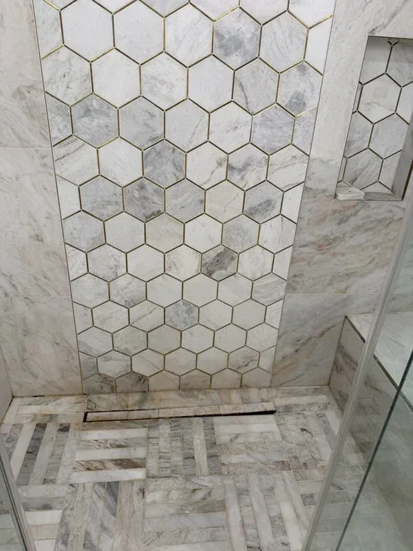 Marble hexagon mosaic shower wall with brass inlay above a basketweave marble floor and linear drain
