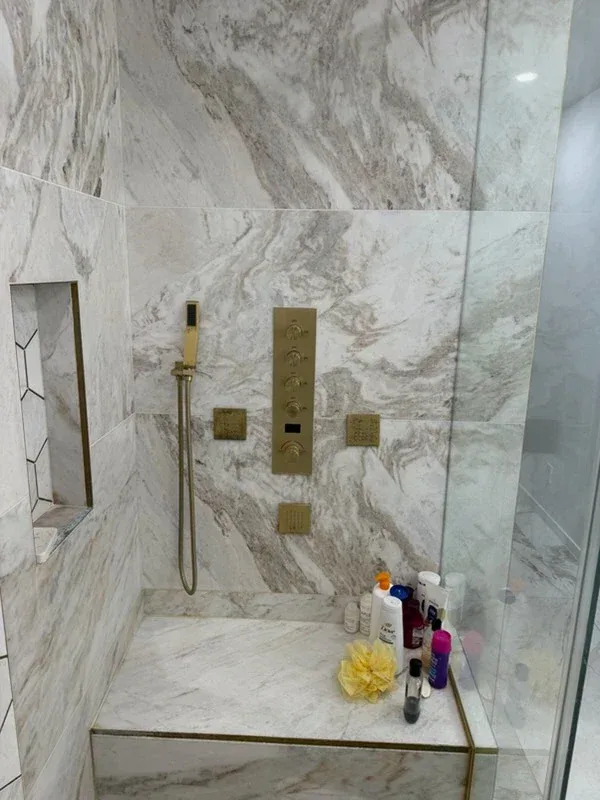 Marble shower with veined slab walls, a marble bench, and brushed brass fixtures