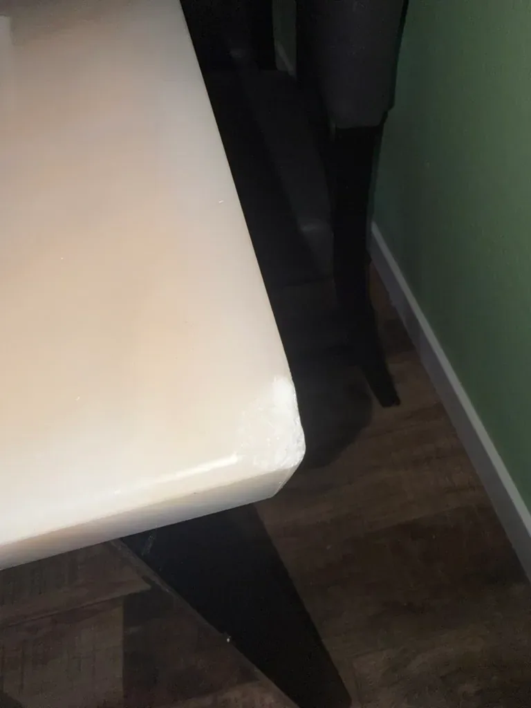Corner of a pale marble table where the stone is crushed white across the top and edge