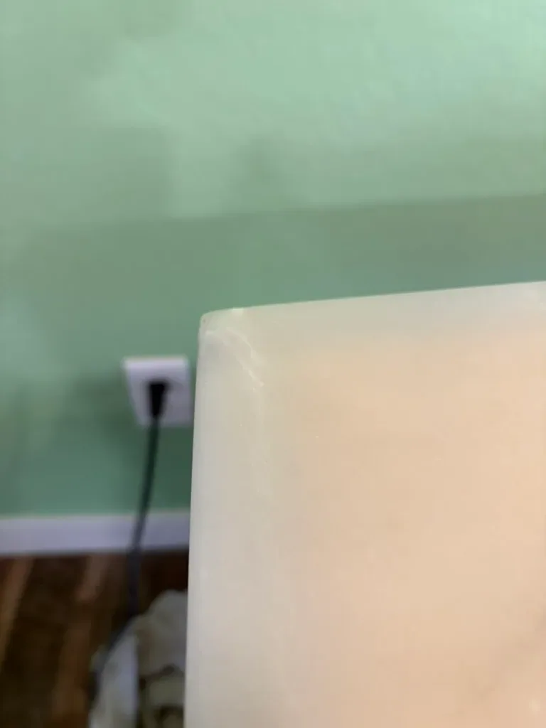 Rebuilt corner of a pale marble dining table, square and sharp, seen from the side