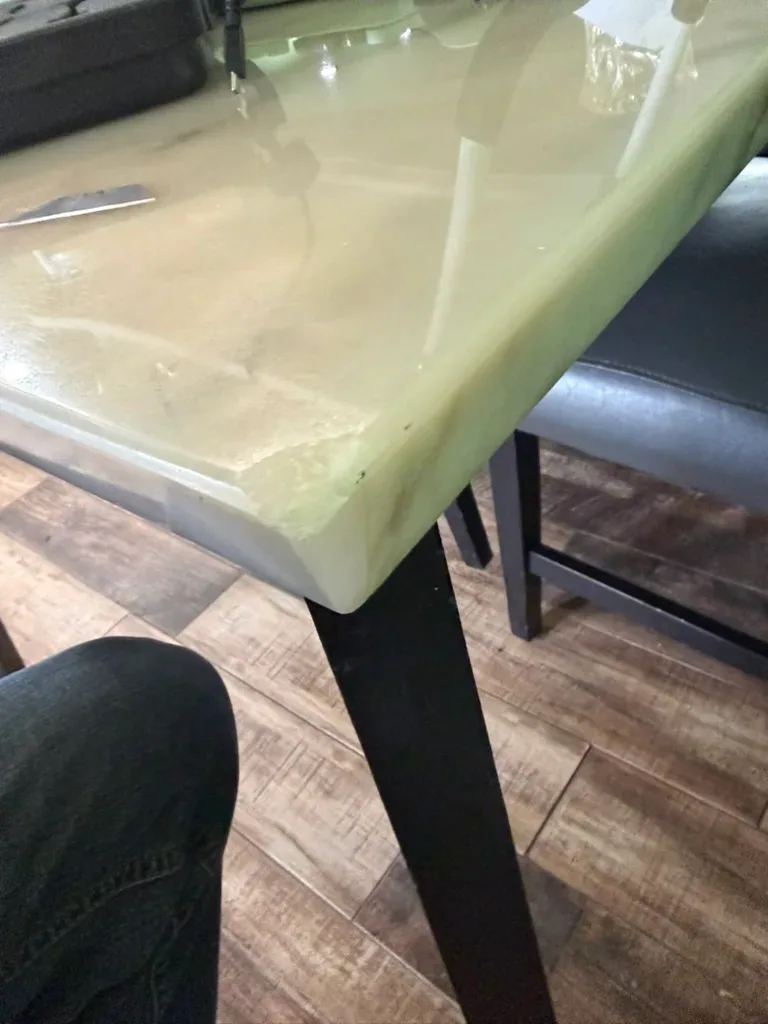 Glossy pale green marble dining table top with a chip along the front edge and light showing through the edge