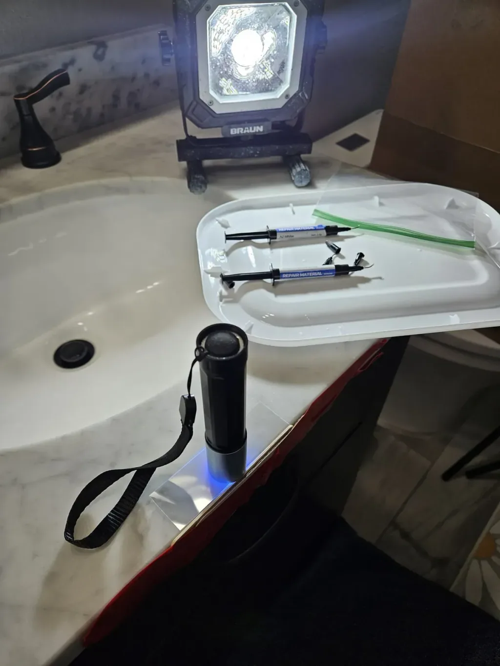 Repair resin, applicators, and a UV flashlight laid out on a white marble vanity beside the sink