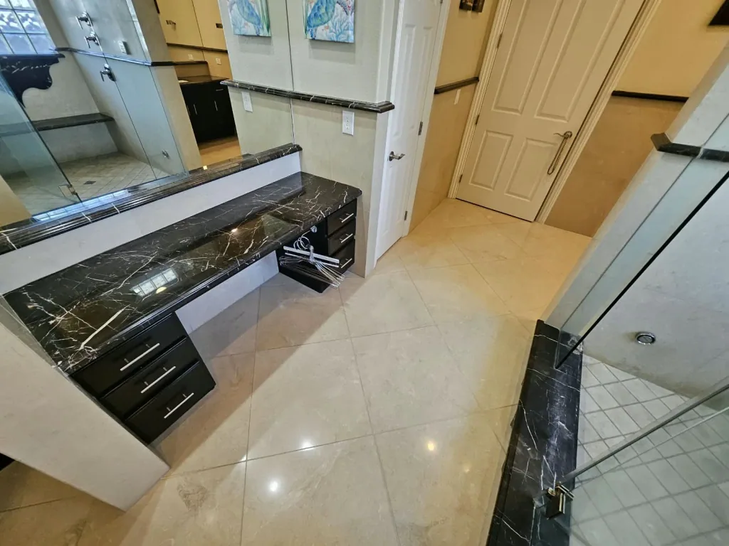 Bathroom with a polished black veined stone vanity top, matching stone trim and a stone shower curb beside a glass shower enclosure