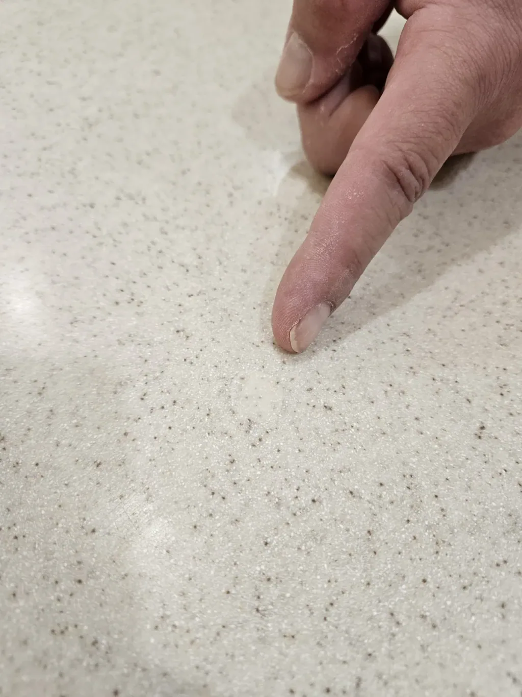 Finger pointing to a filled and leveled chip in the same speckled quartz countertop