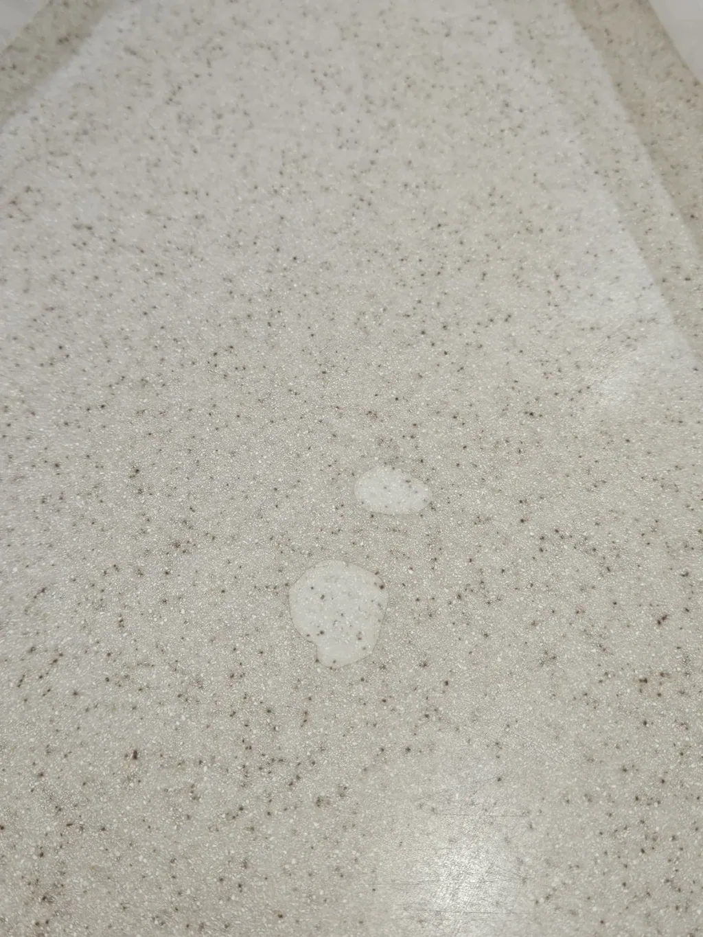 Two light chipped spots in a speckled cream quartz countertop