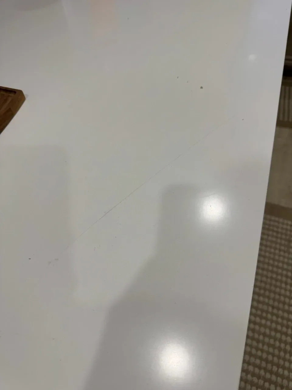 Fine curved scratch crossing a white quartz countertop, visible in the glare of the kitchen lights