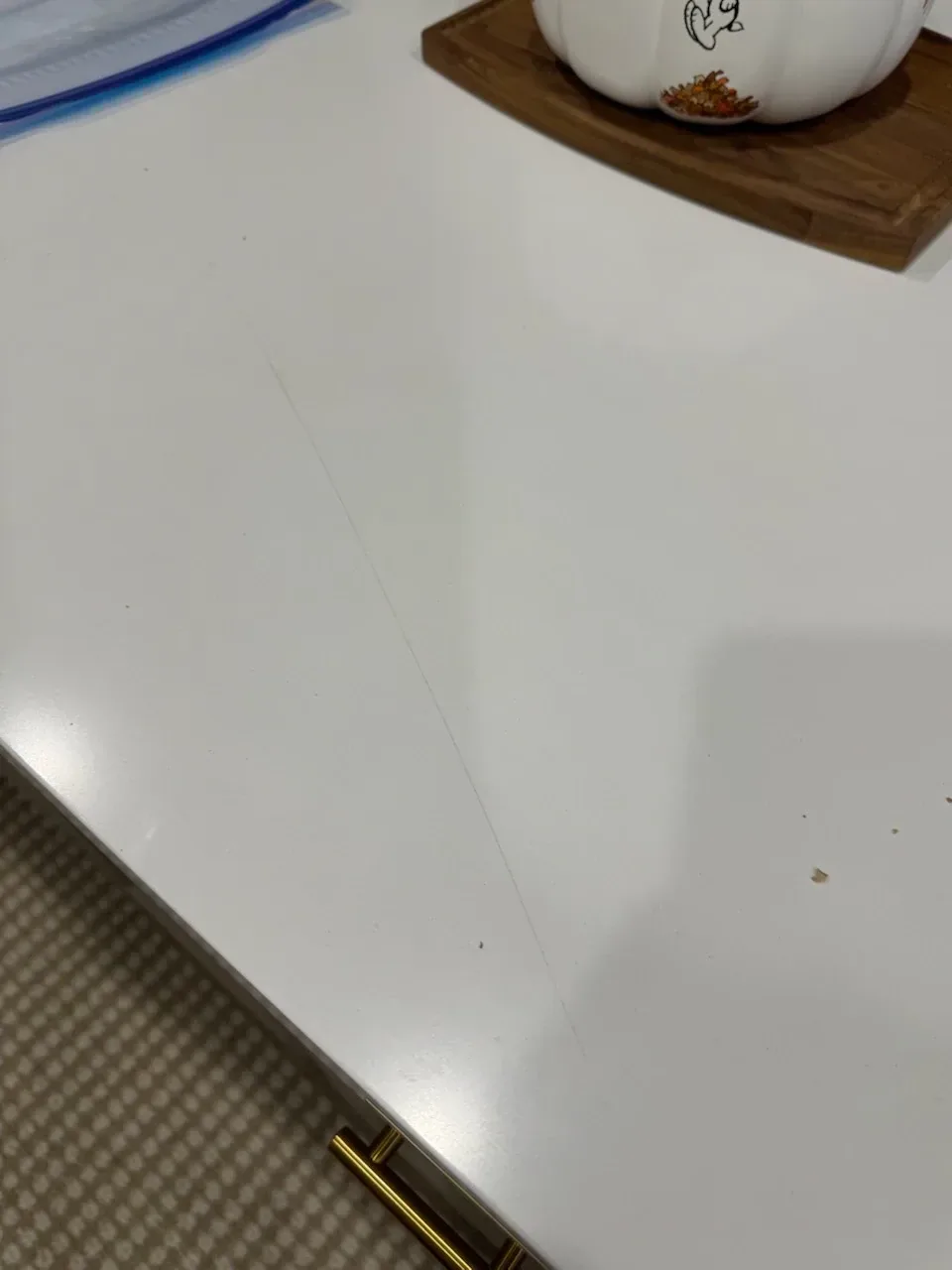 Long fine scratch running across a white quartz kitchen countertop toward the front edge