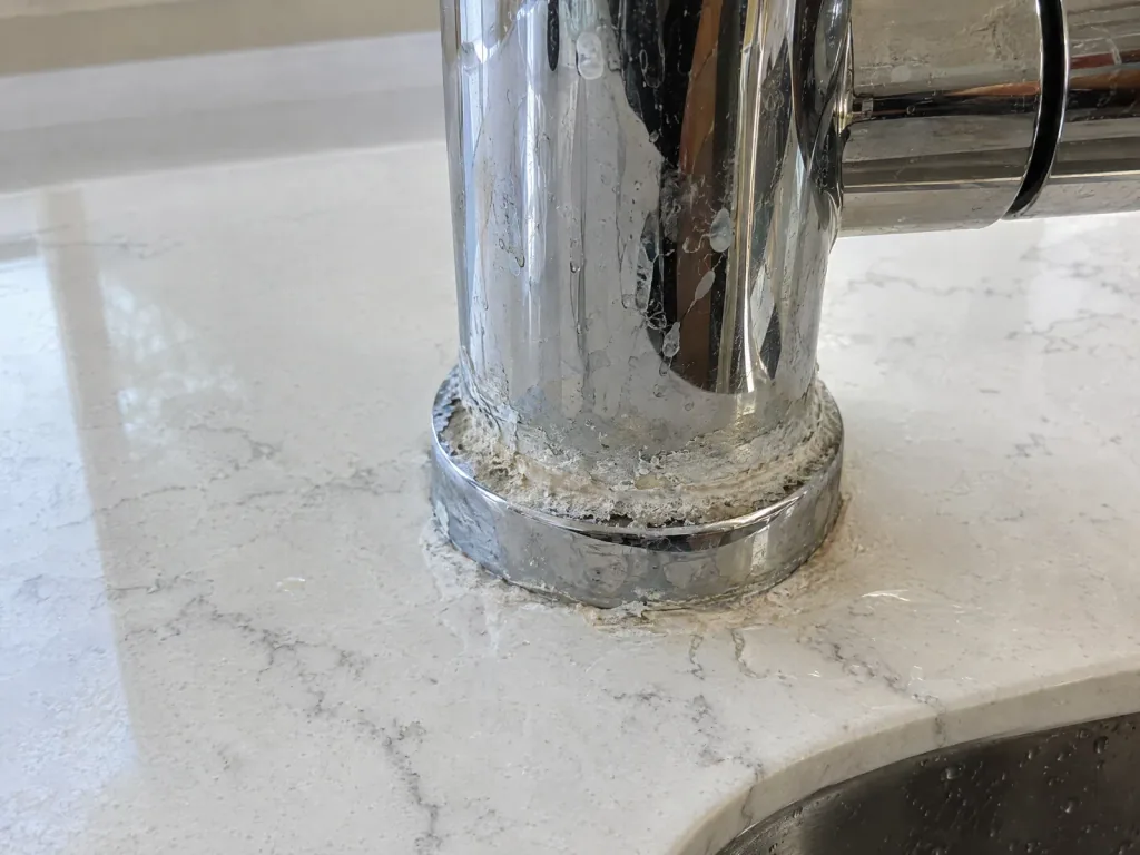 White ring of hard-water scale on a quartzite countertop around the base of a kitchen faucet