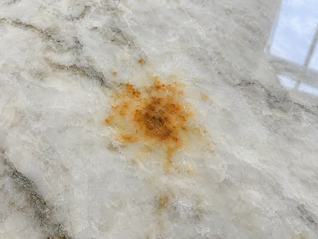 Small orange rust spot blooming from inside a pale quartzite countertop