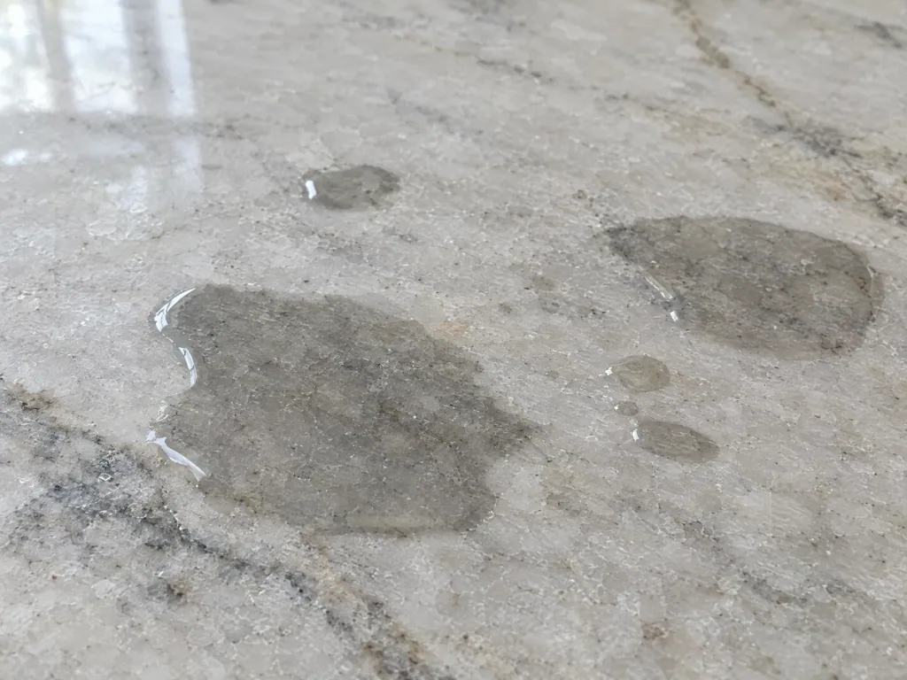 Water drop test on unsealed quartzite, with a dark wet patch spreading into the stone around the drops