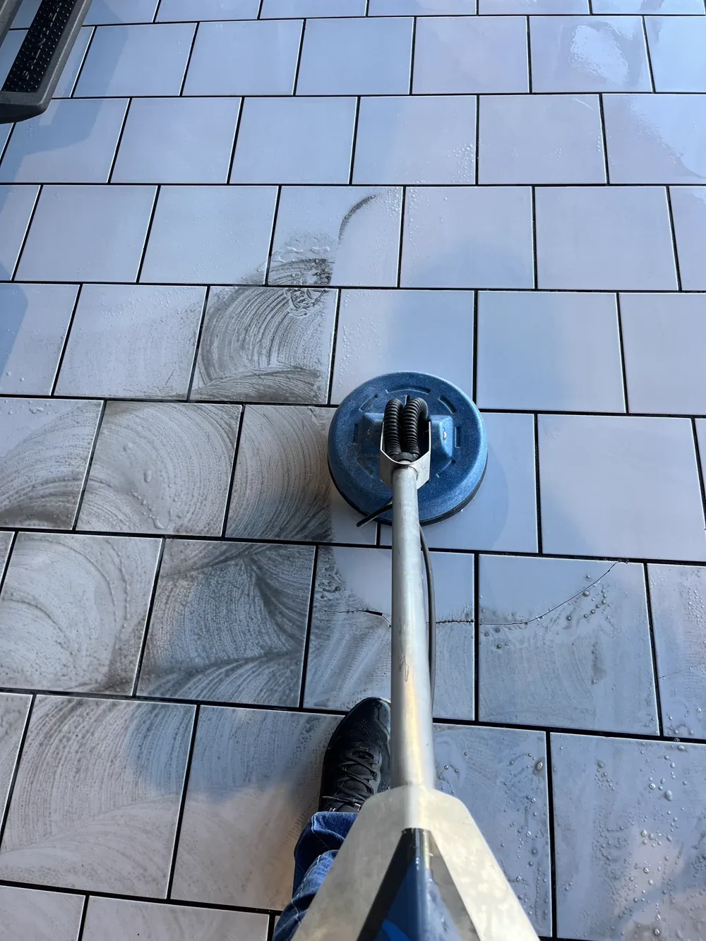 Enclosed rotary extraction tool moving across a white tile floor with soiled solution being pulled out of the joints