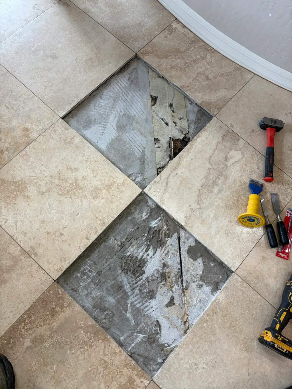 Two cracked travertine tiles removed from a diagonal floor, exposing the thinset bed and a mesh membrane below