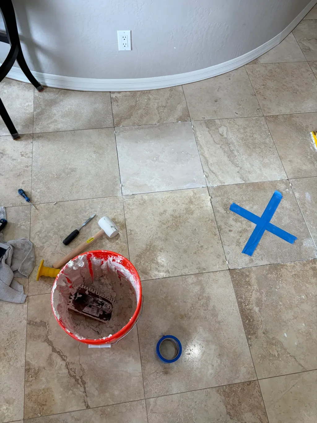 Replacement travertine tile set into the floor beside a bucket of thinset and setting tools