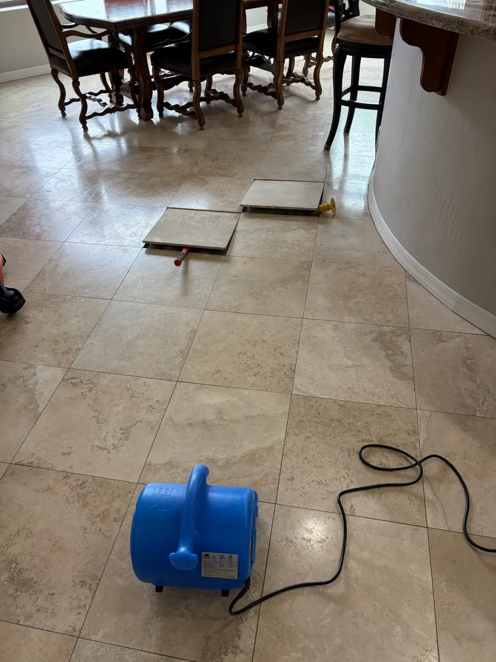 Travertine tiles lifted with suction cups during a replacement, with an air mover drying the floor in front