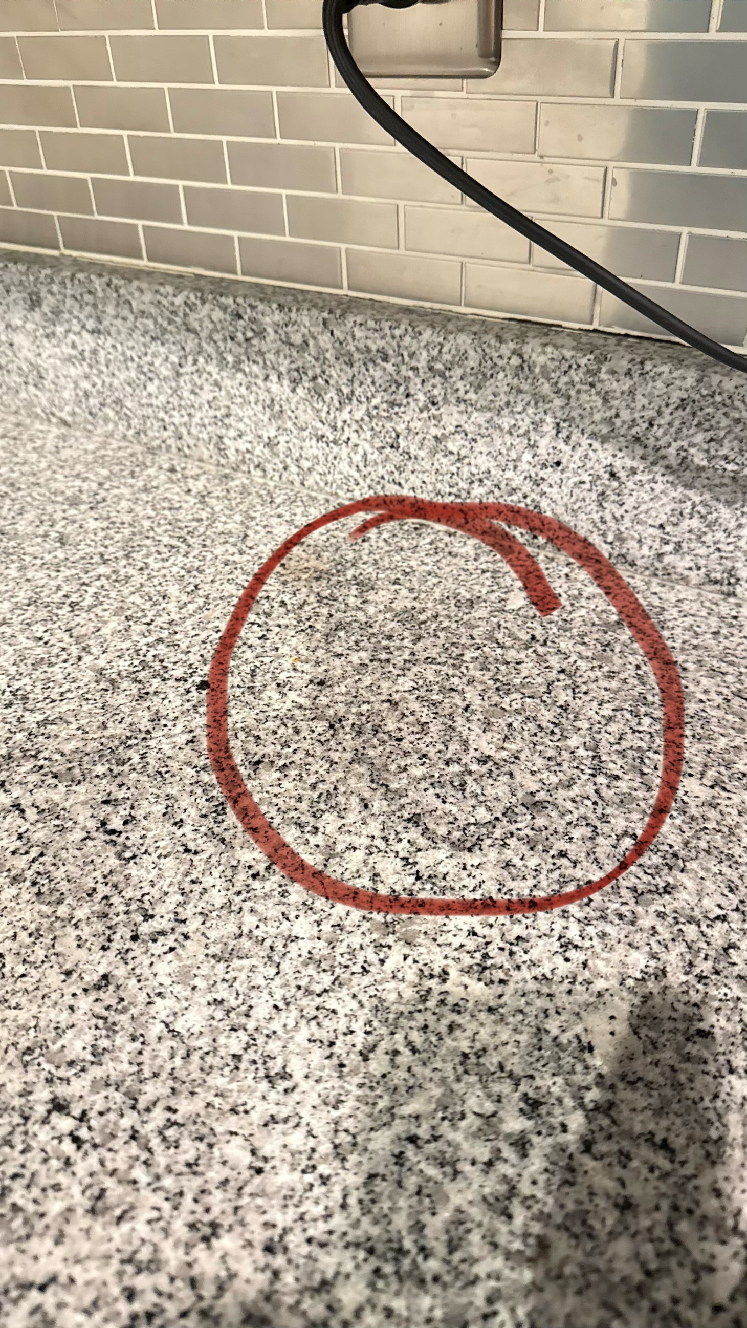 Dark area on a speckled granite countertop where an espresso machine sat, marked with a red circle