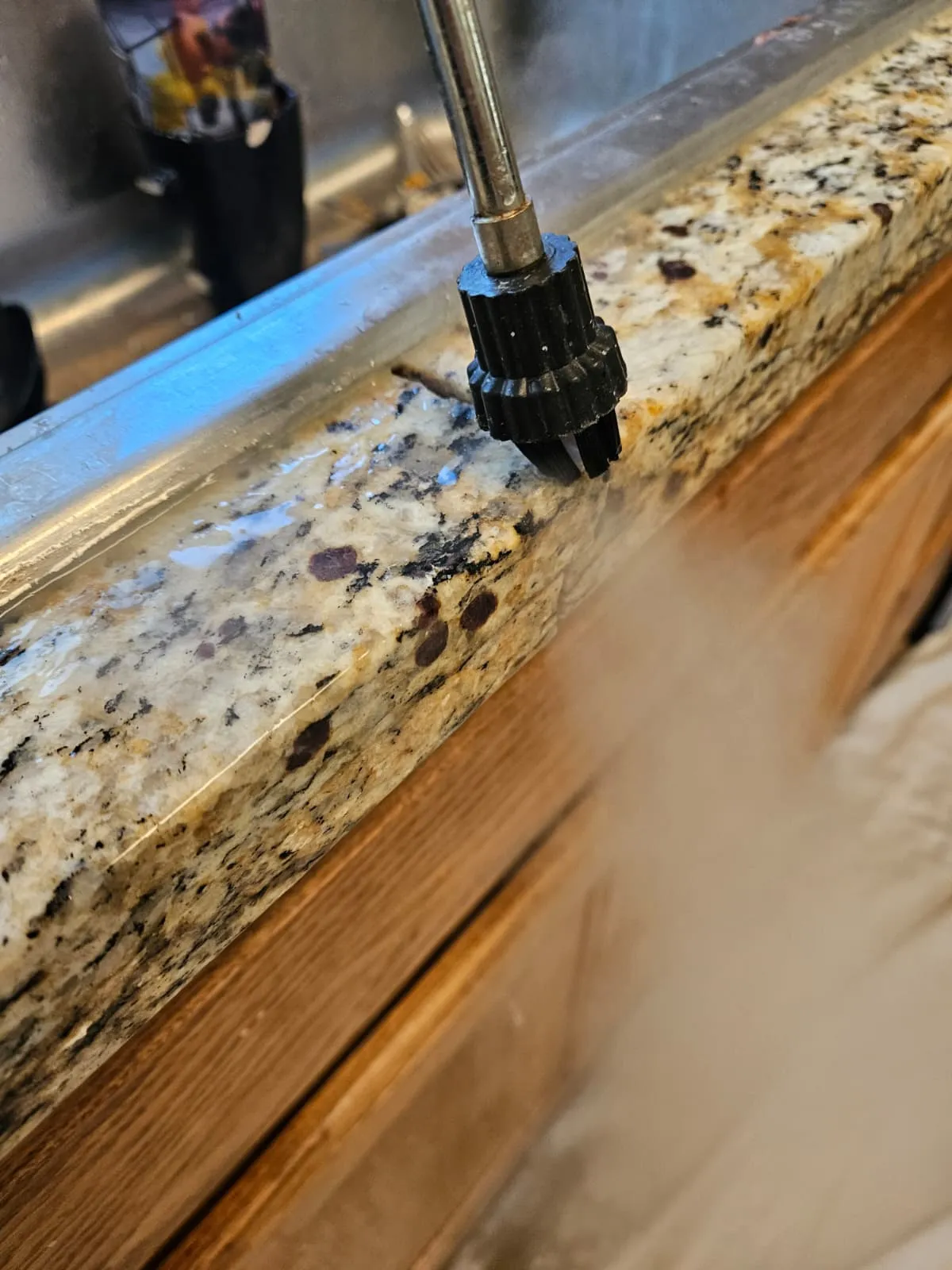 Close view of a granite countertop being steam cleaned beside a sink