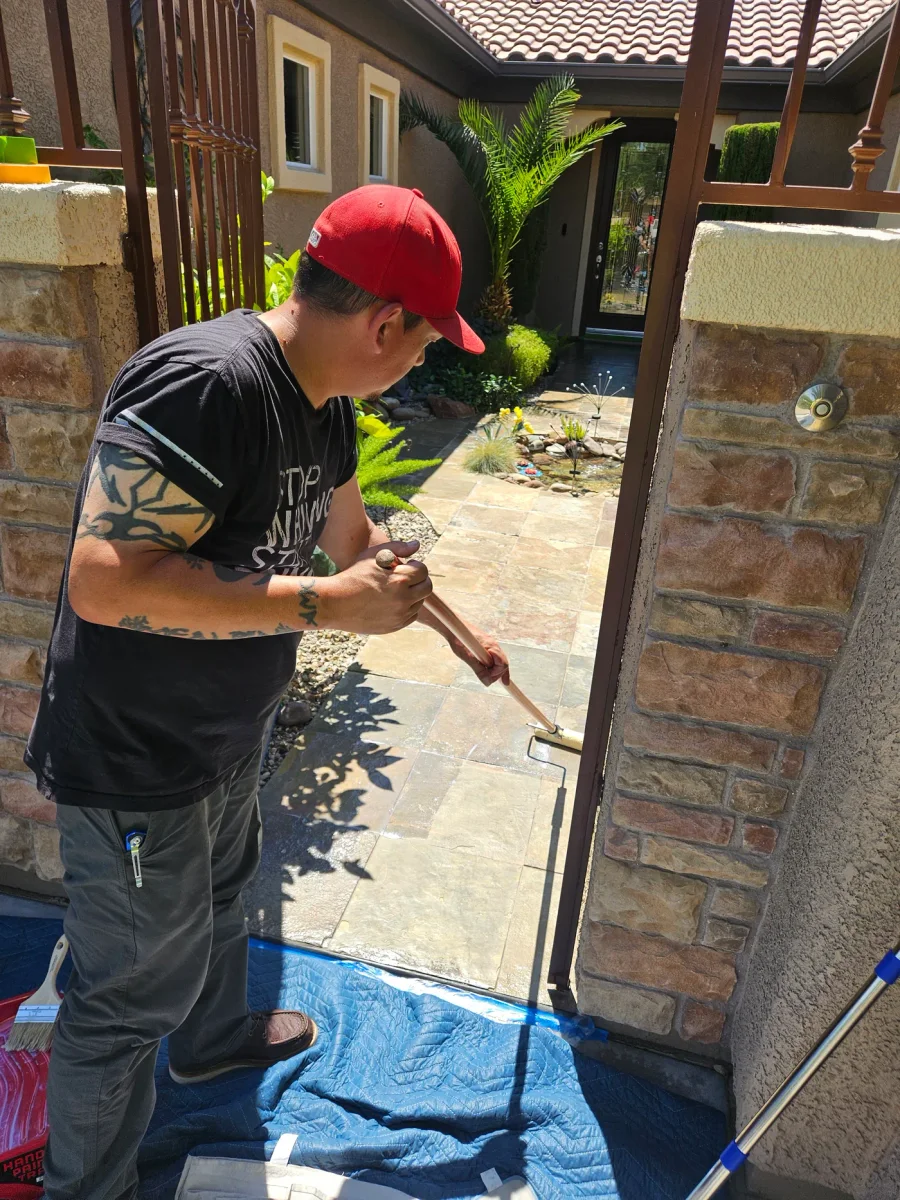 Technician applying paver sealer with a pole applicator along a stone walkway, drop cloth down at the gate