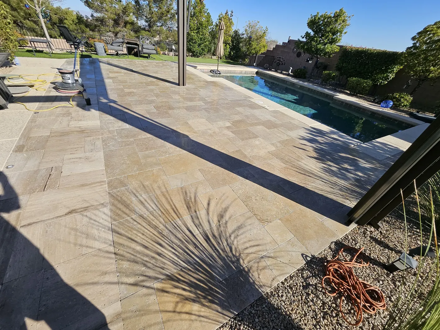 Travertine pool deck being machine cleaned beside a backyard swimming pool