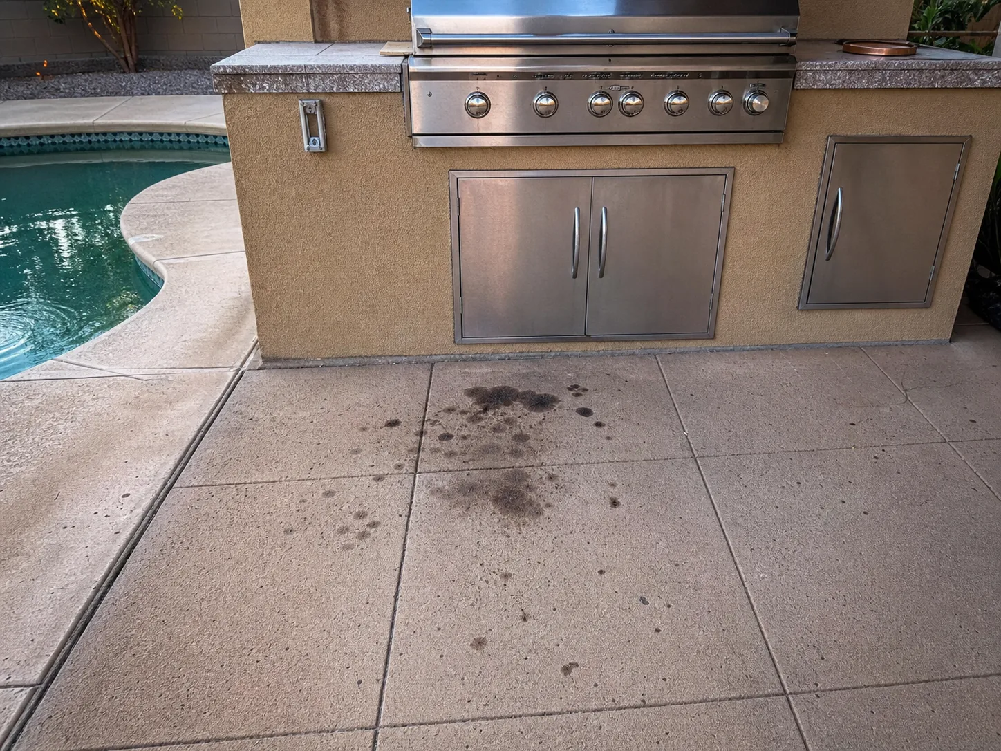 Oil and grease stains on a pool deck in front of an outdoor barbecue