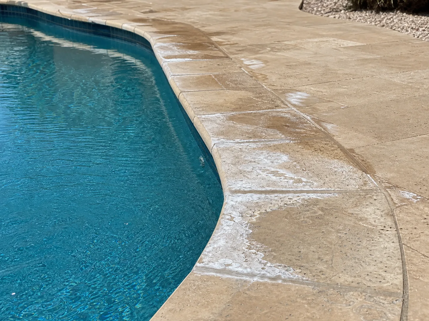 White hard-water mineral crust around a travertine pool coping and splash line