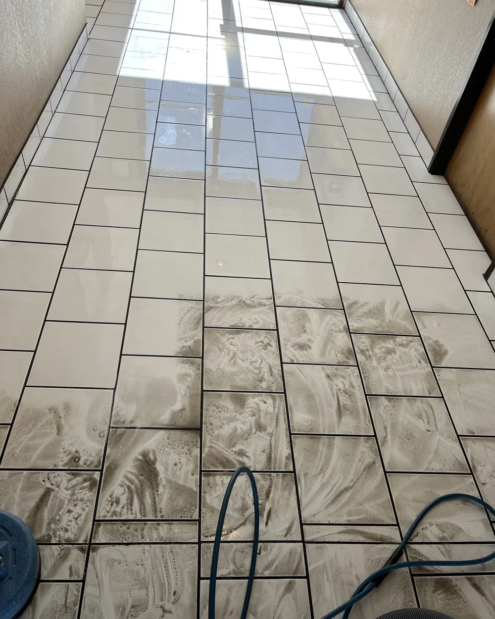 Hard floor being deep cleaned mid-job, residue lifting away from the tile and its joints