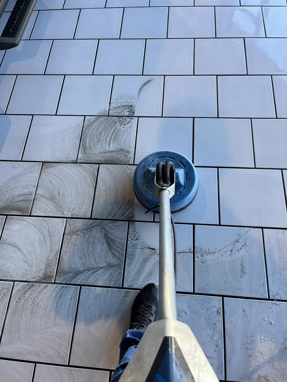 Enclosed rotary extraction tool lifting soil out of a white tile floor and its grout joints