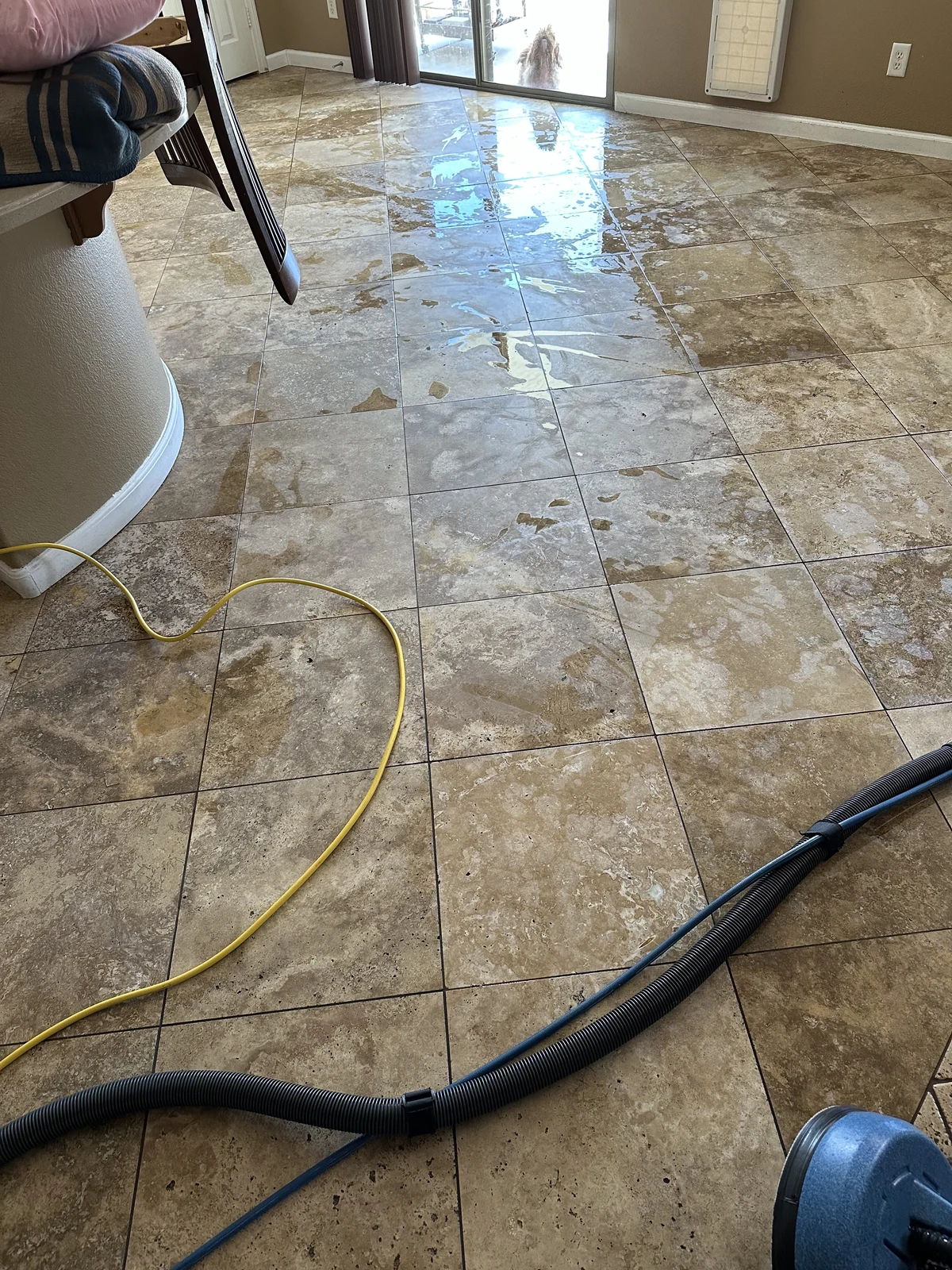 Natural travertine floor with restoration hoses and wet work equipment in a residential room